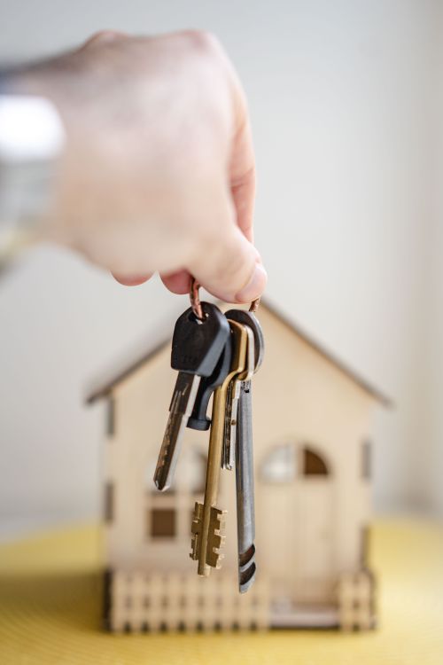 House keys held beside a small wooden model of a building