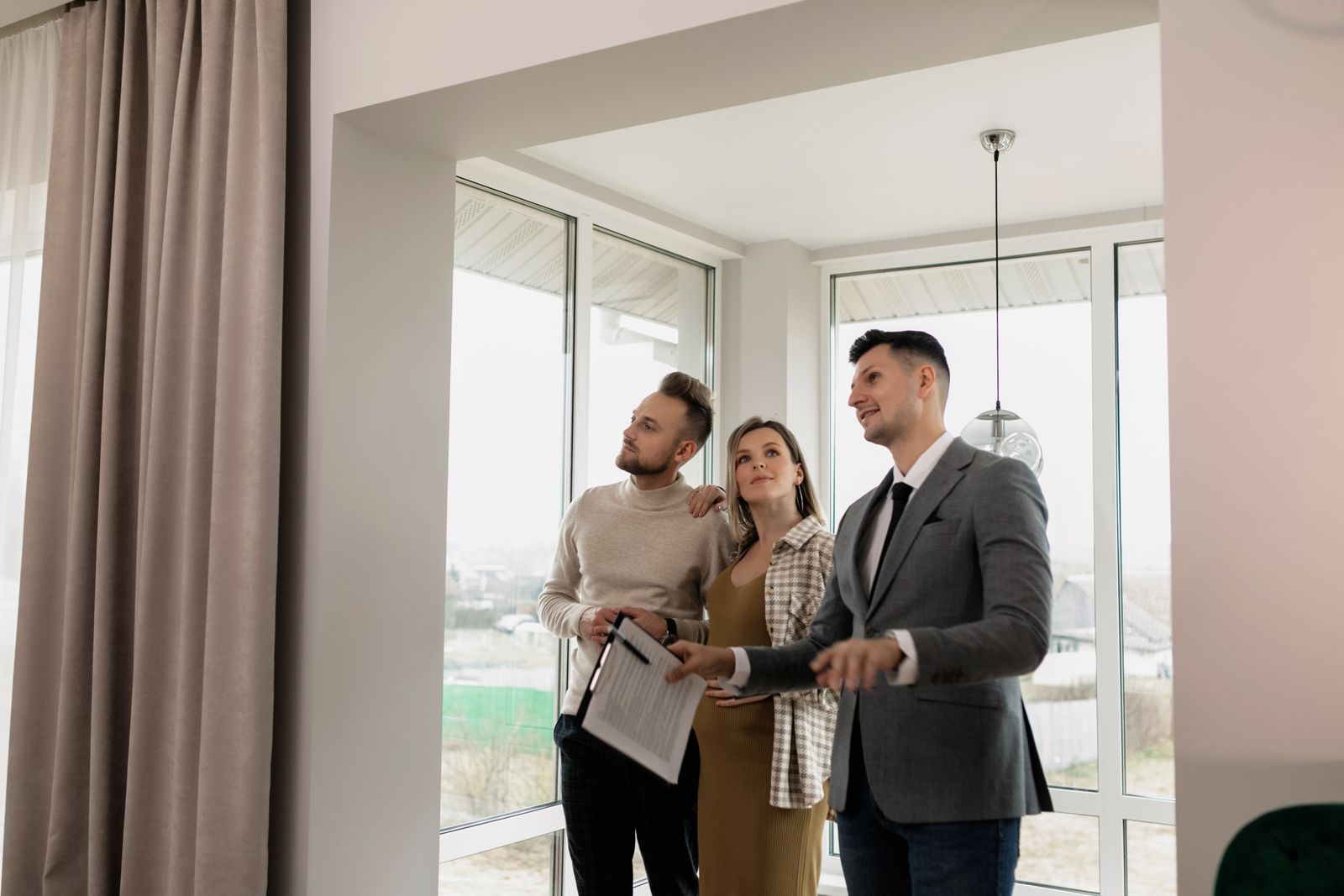 A real estate agent showing a modern home to a young couple during a daytime viewing
