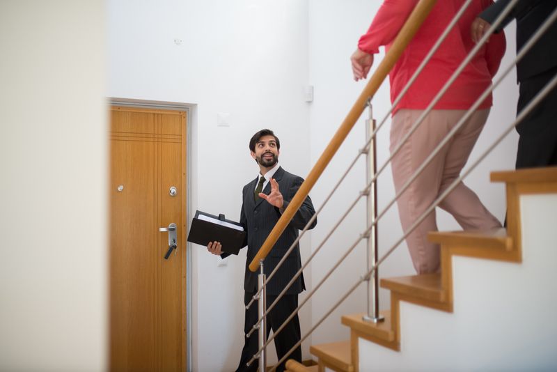 A buyer's agent conducts a property showing with clients on the stairs of a modern home