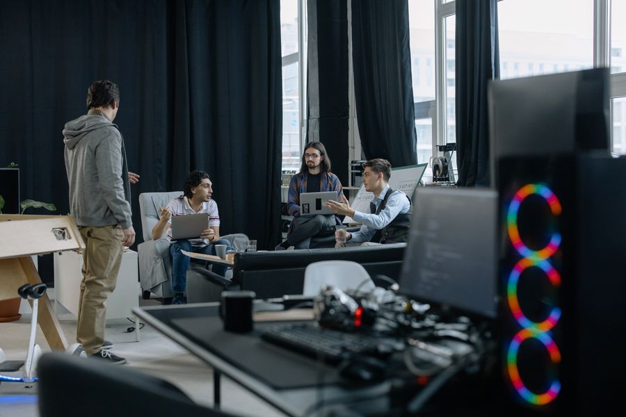 A group of professionals in a casual meeting at a modern office, discussing projects on laptops and tablets