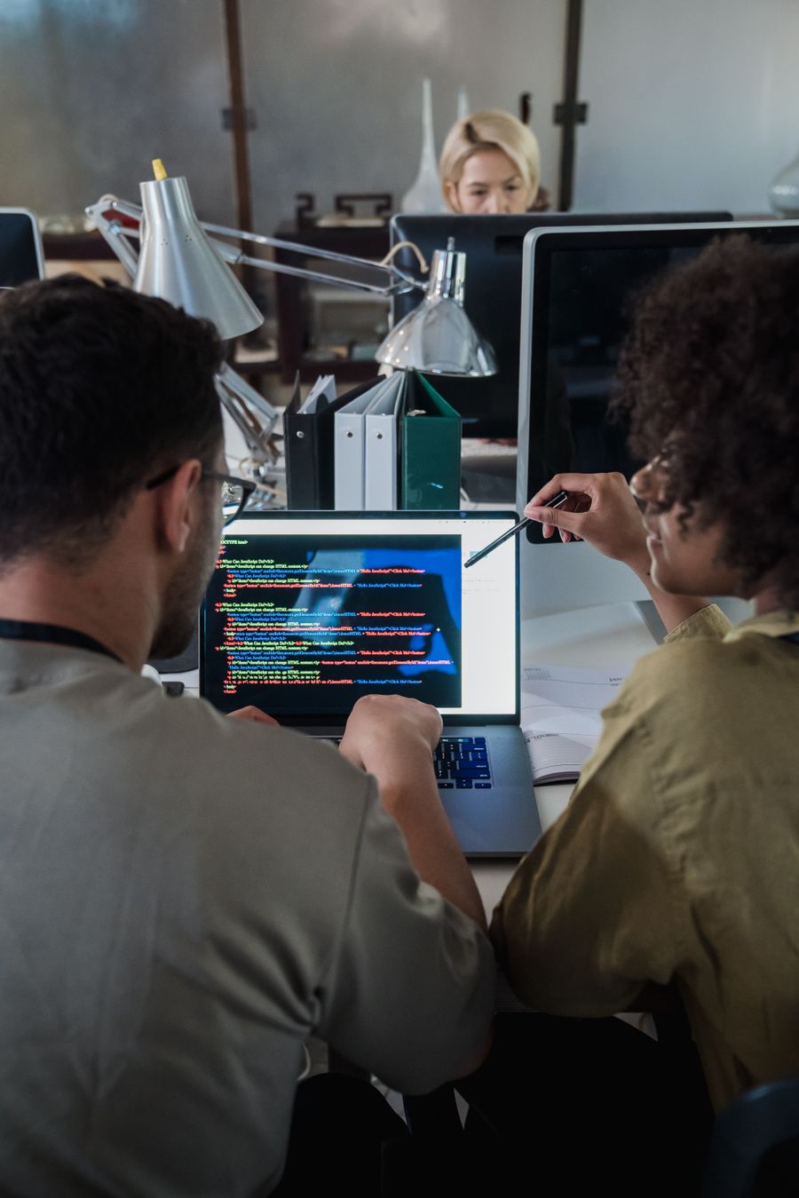 Two developers working through software code together on a laptop in a modern office