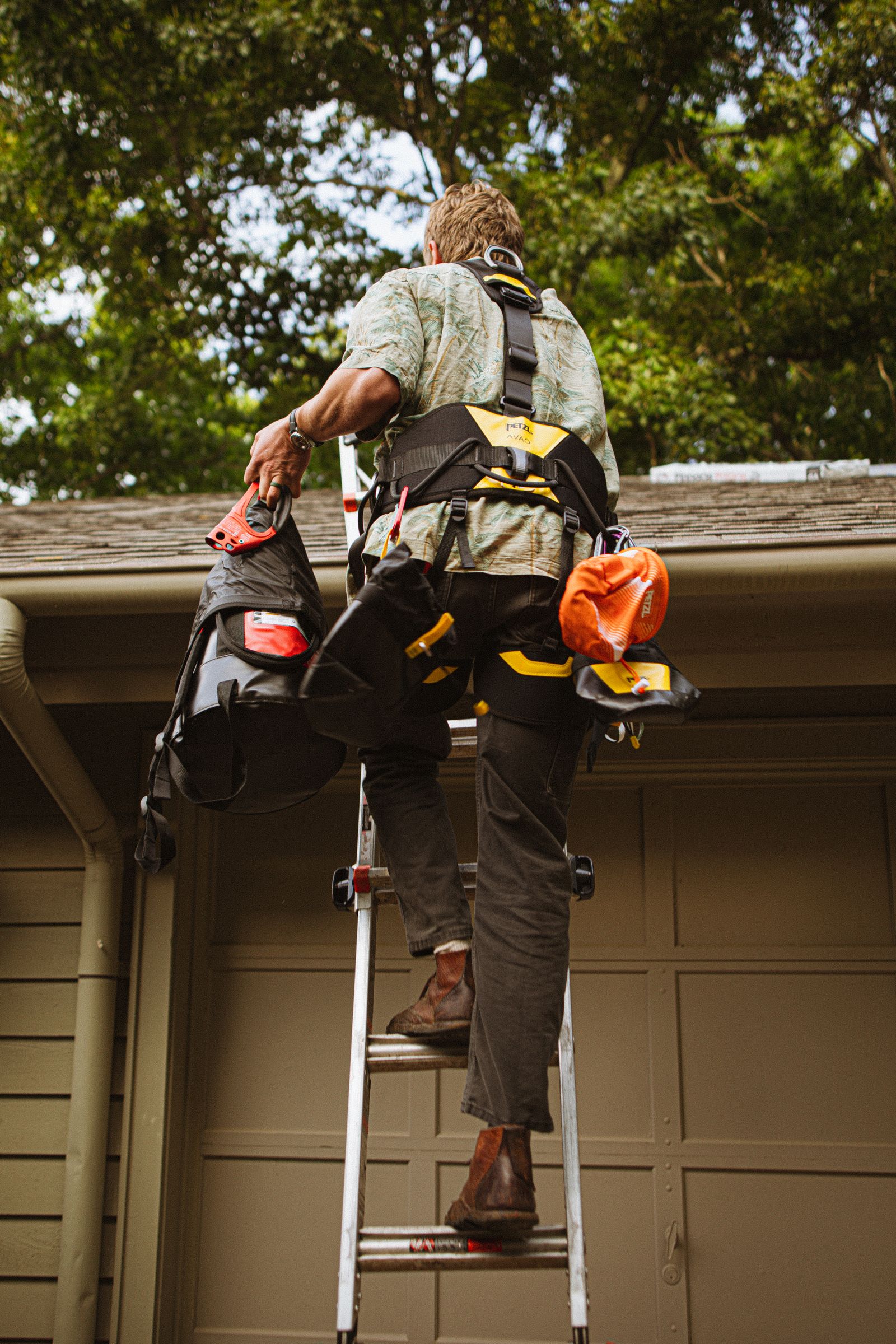 A construction worker in safety gear climbing a ladder to carry out roof repairs on a house