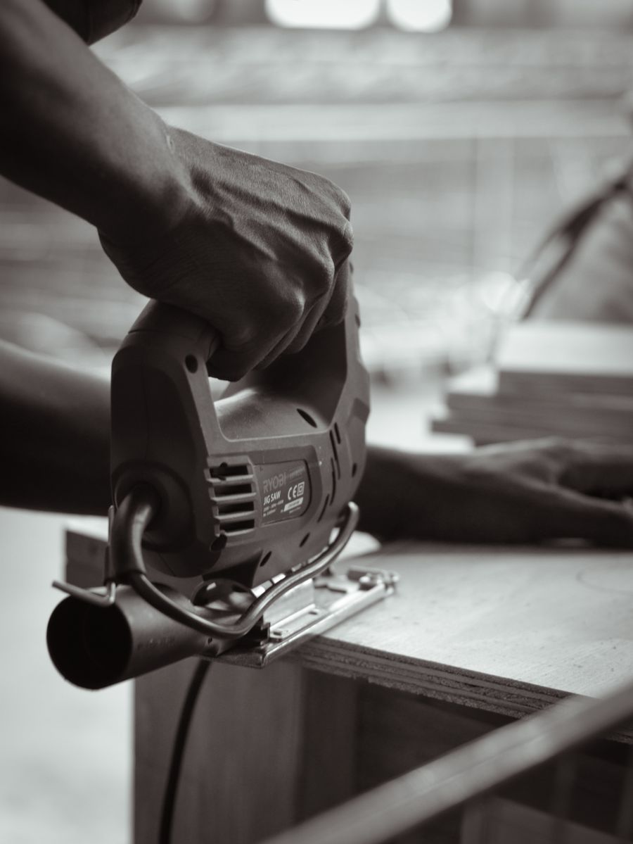 Black and white photograph of a carpenter guiding a jigsaw through a piece of timber indoors