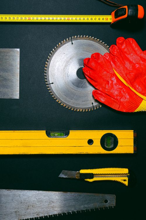 Construction tools including a saw blade and work gloves laid out on a black surface