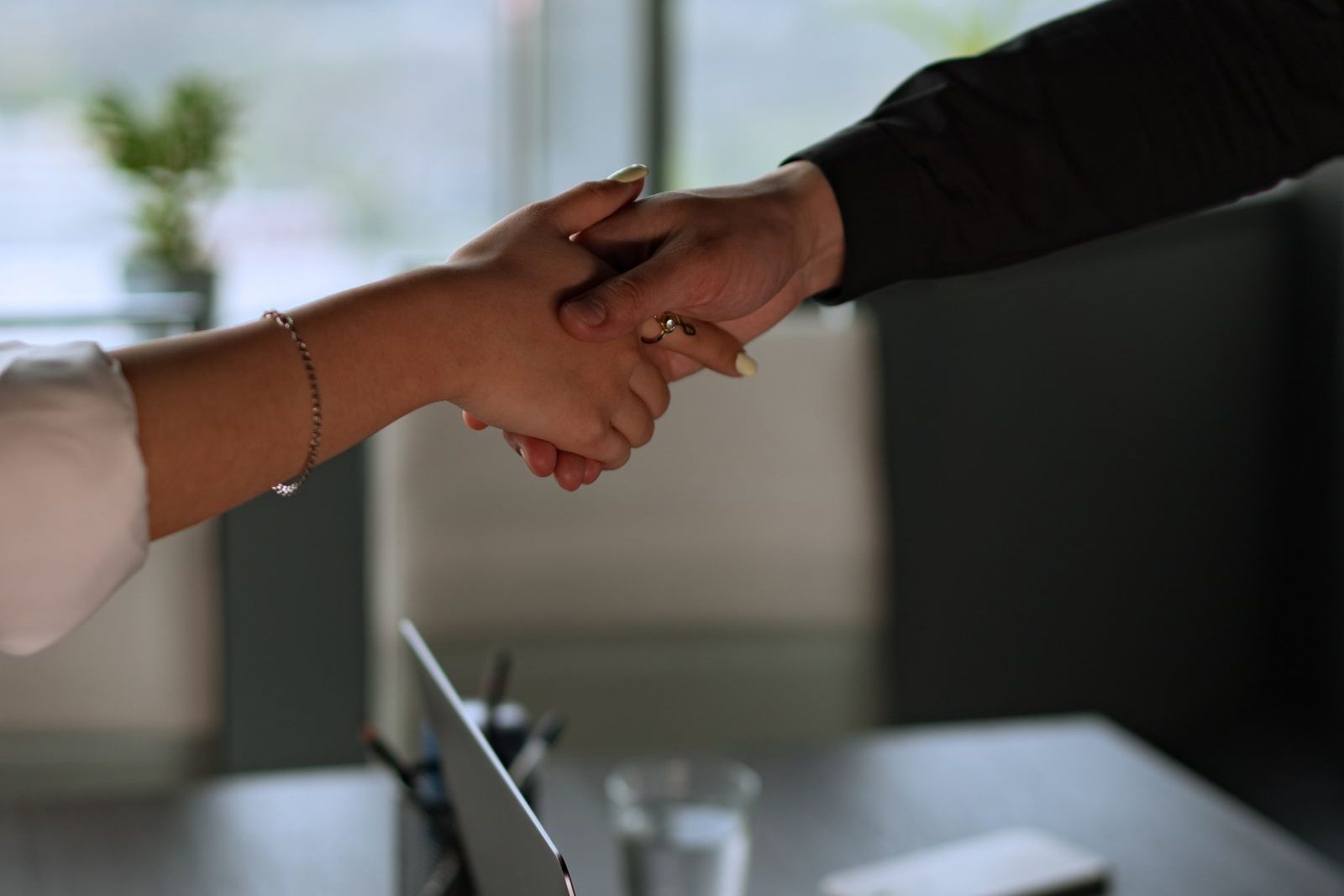 A mortgage broker and client shaking hands across a desk in a bright, modern office