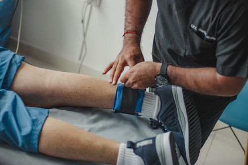 A physiotherapist adjusting a strap around a patient's leg during a clinical treatment session