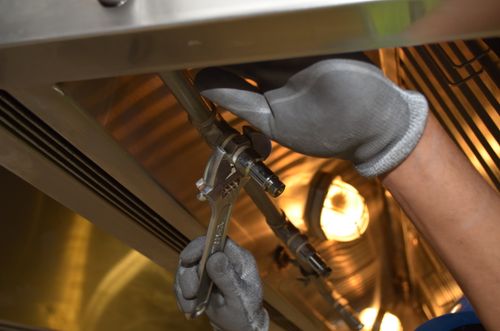 Gloved hand using pliers on a stainless steel kitchen exhaust duct fitting