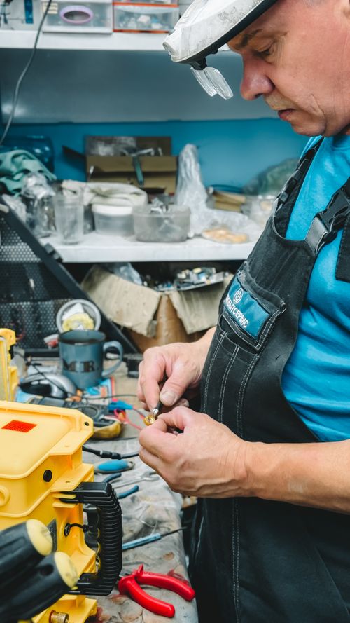 Technician in overalls repairing electrical equipment beside a toolbox