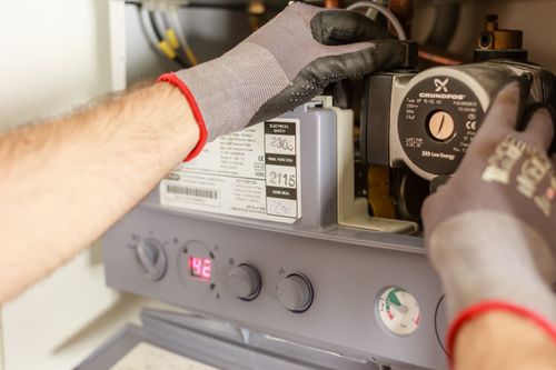 Gloved hands adjusting the dials on a home heating boiler unit