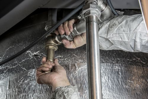 Hands fitting a pipe connection beneath a sink