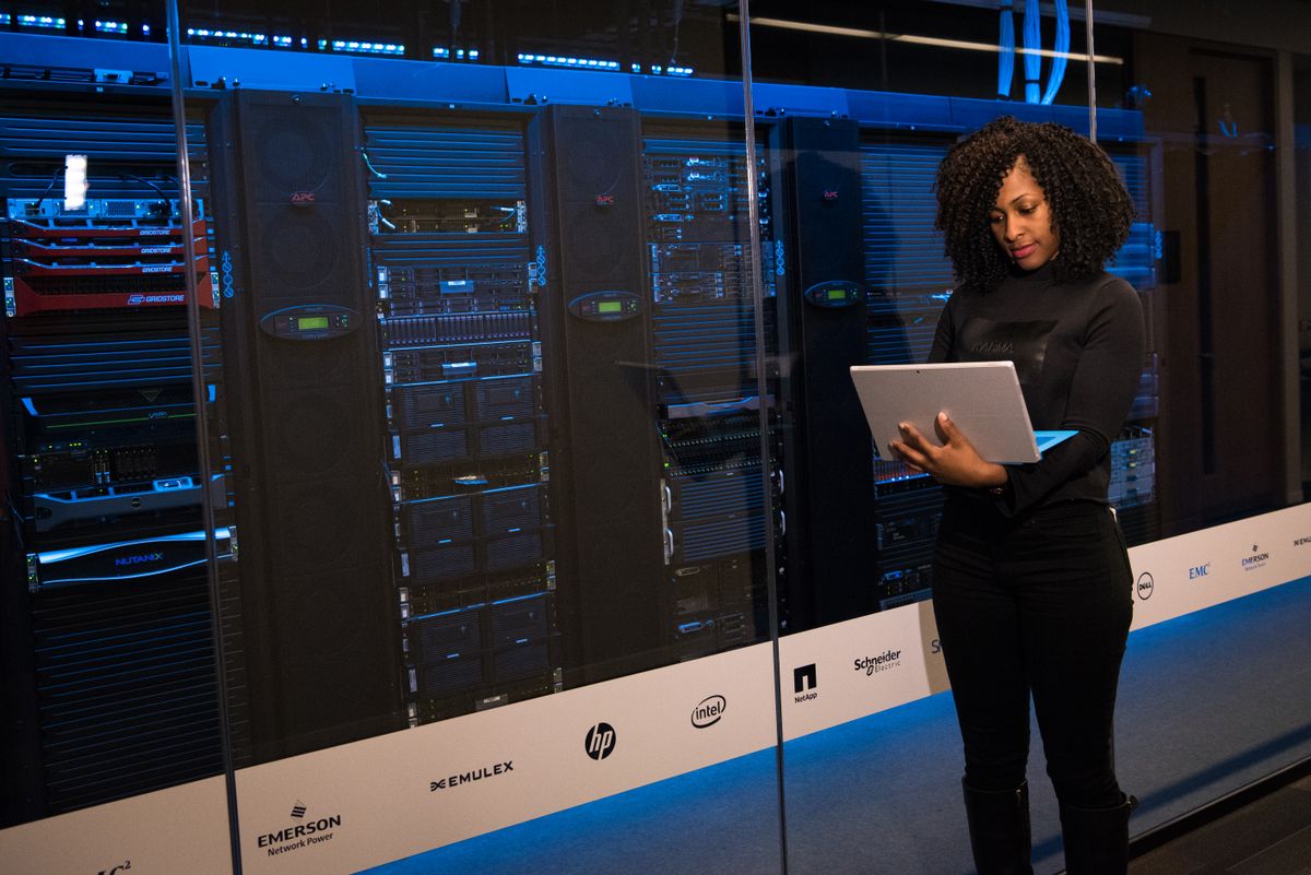 An engineer checking a laptop while monitoring racks in a server room