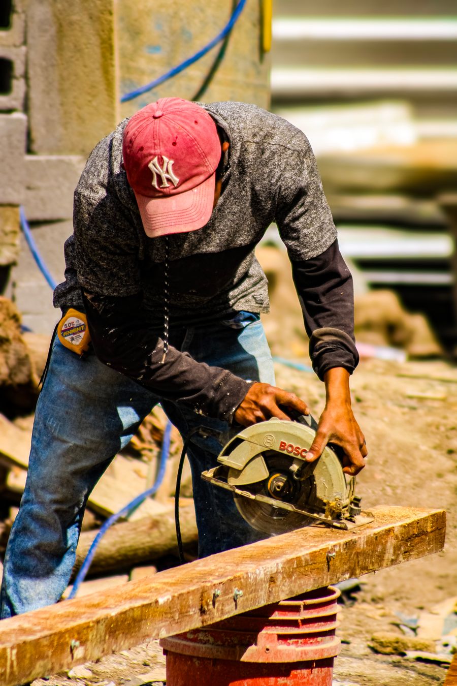 A carpenter using a circular saw to cut a wooden plank outdoors