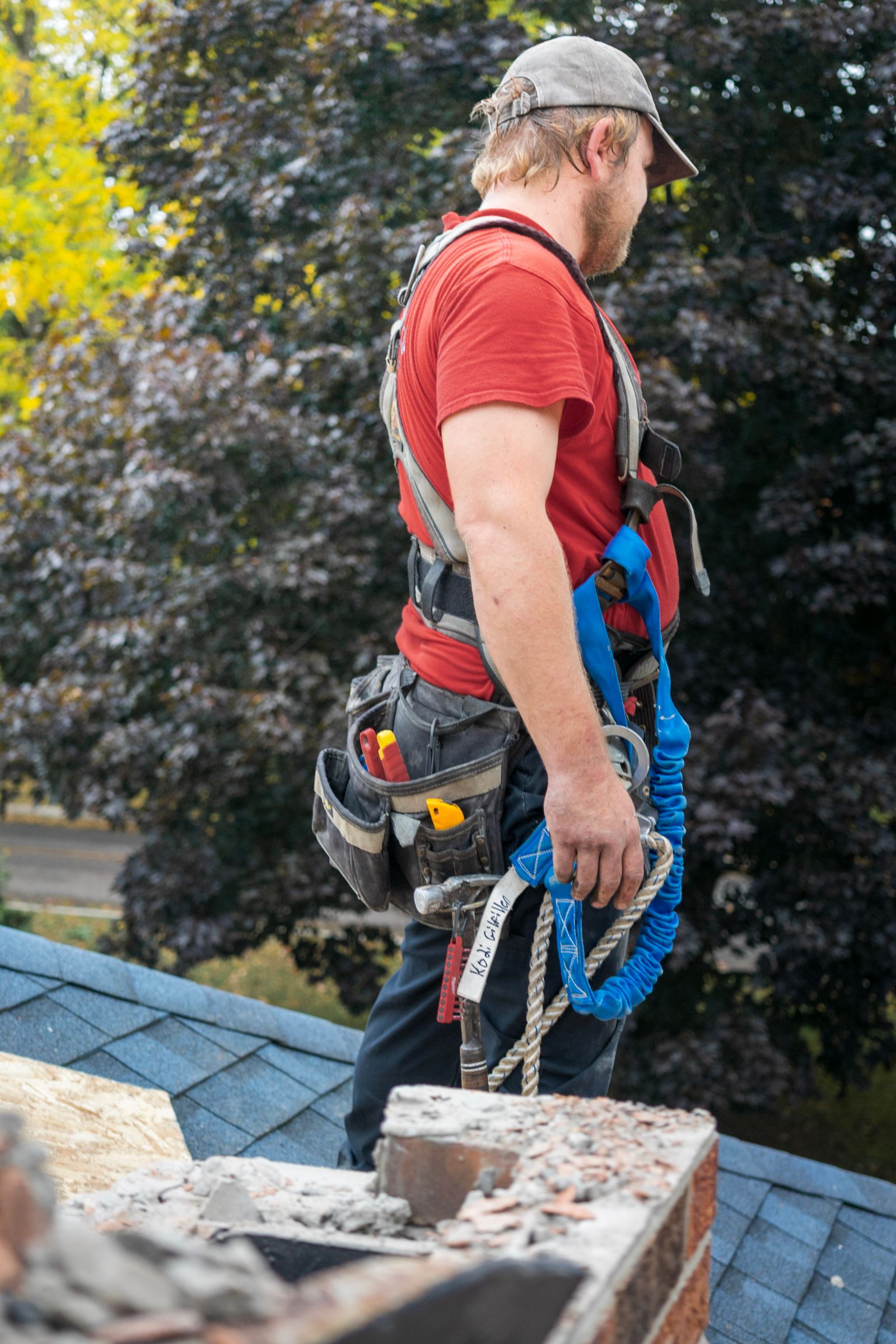 A worker in safety gear standing on a residential rooftop inspecting a chimney