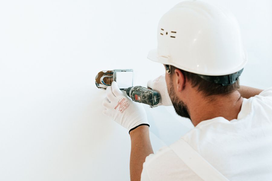 Tradesperson in a hard hat and work gloves using a power tool to repair a wall