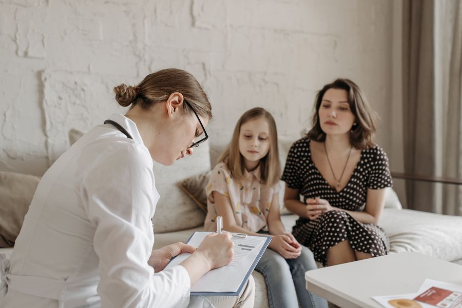 A doctor speaking warmly with a mother and daughter in a bright consultation room